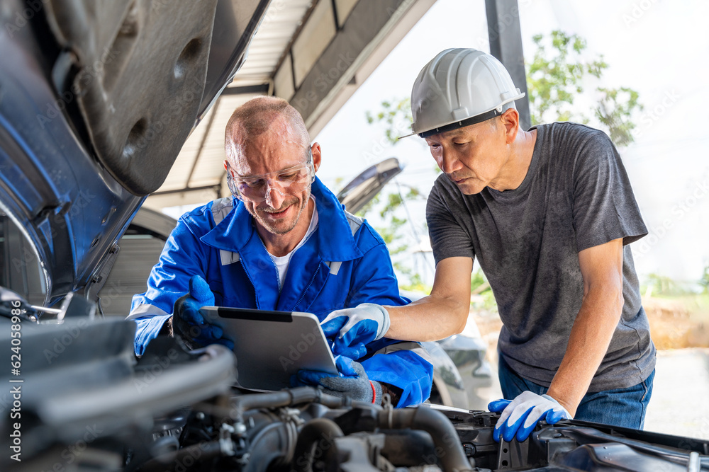 Two auto mechanics using a computer tablet while working together on the car engine at car repair garage