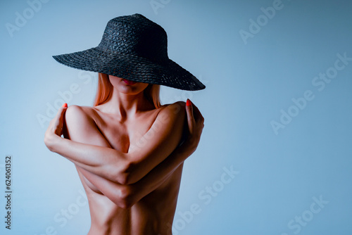 Beautiful young nude woman in a hat posing in the studio.