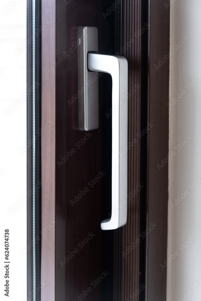 Aluminum silver handle on close door, window against brown frame background. Close up view. Vertical Aluminum silver handle on close door, window against brown frame background. Close up view. Vertical