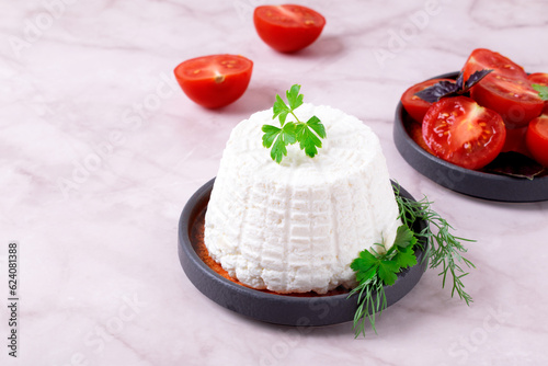 Fresh ricotta cheese topped with parsley served with cherry tomatoes on white table. Italian cuisine