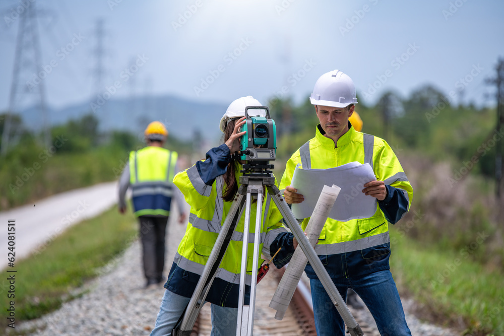 Surveyor engineers team wearing safety uniform,helmet and blueprint document checking inspection by theodolite to measurement position on railway construction site is industry transportation concept. - obrazy, fototapety, plakaty 