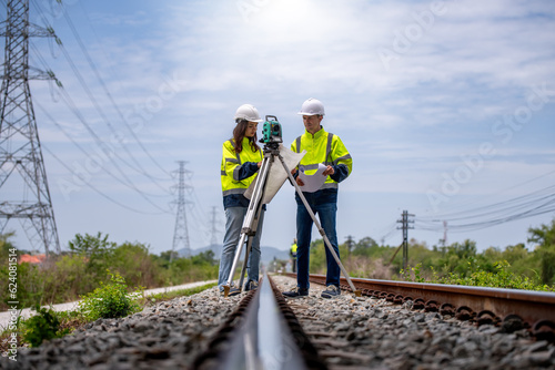 Canvastavla Surveyor engineers team wearing safety uniform,helmet and blueprint document checking inspection by theodolite to measurement position on railway construction site is industry transportation concept