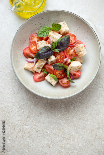 Plate of italian panzanella salad on a beige stone background, vertical shot with space, above view
