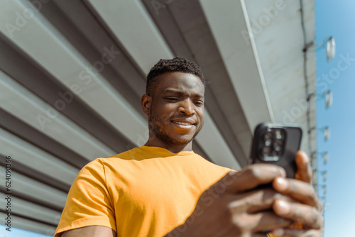 Portrait of young African American man holding mobile phone ordering online shopping on urban street