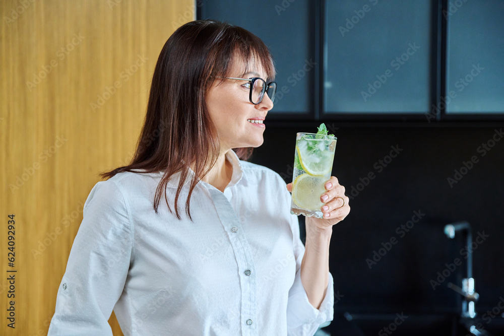 Mature woman drinking glass of water with lemon ice mint Mature woman drinking glass of water with lemon ice mint