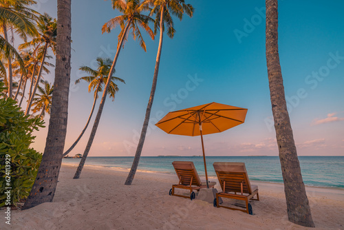 Beautiful tropical sunset coast  two sun beds chairs umbrella under palm trees. Closeup white sand  sea view horizon colorful twilight sky calm and relaxation. Inspire beach resort wellbeing landscape