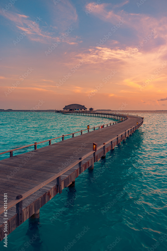 Maldives island sunset. Water bungalows villas resort at islands beach. Indian Ocean, Maldives. Long wooden pier path in luxury resort. Colorful sky sea clouds, calm relax nature. Peaceful reflections
