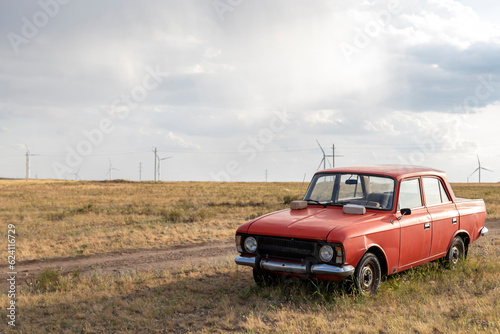 an abandoned car against the backdrop of a windmill with huge blades somewhere in the steppe of Kazakhstan