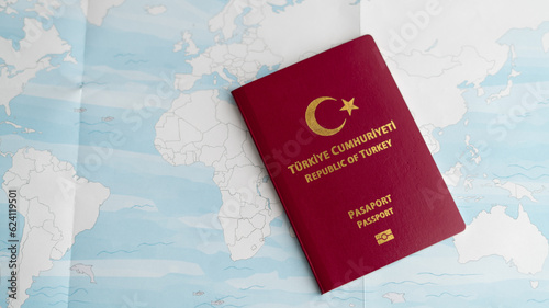An up-close photograph displaying a Turkish passport placed atop a world map, showcasing the words "Republic of Turkey" and "Passport" in the Turkish language.