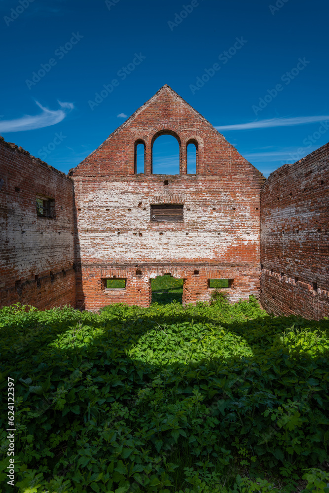 Red brick walls of an old building without a roof against a blue sky and green grass.