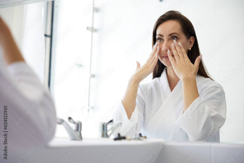 young woman looking at mirror and touching face in bathroom young woman looking at mirror and touching face in bathroom