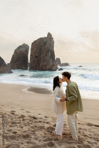 Barefoot beach romance. Loving young couple holding hands and kissing  enjoying date and time together on the beach