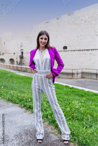 Young woman standing in a park wearing light dress and fuchsia jacket