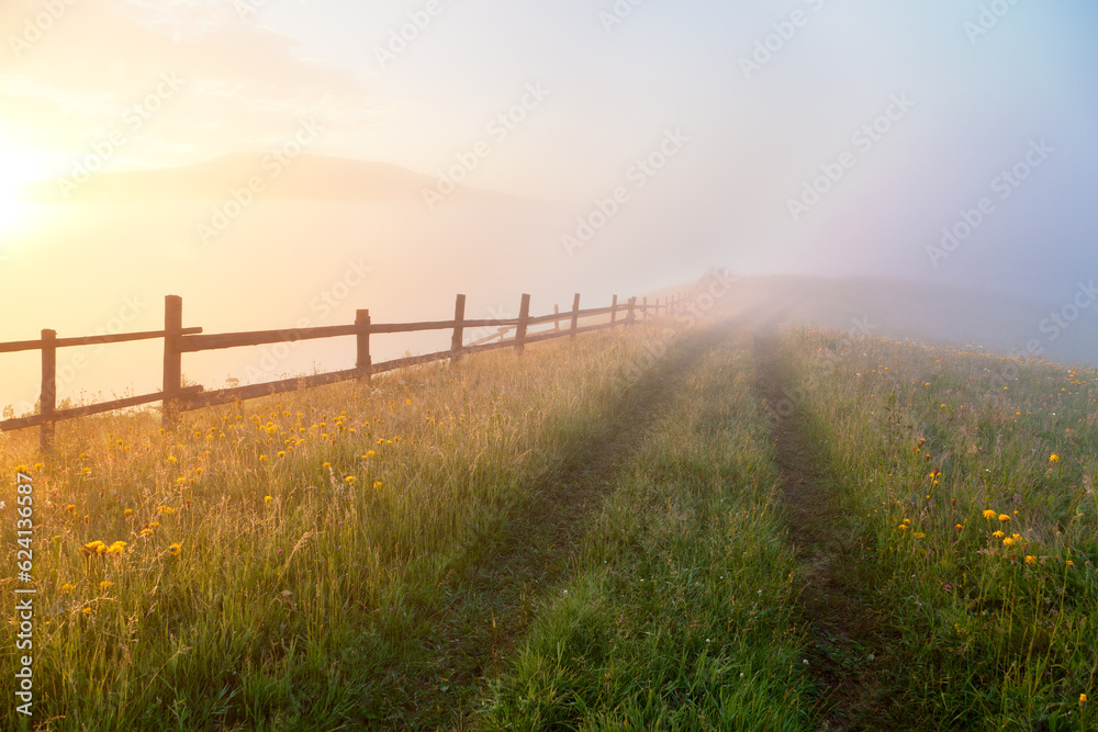 Sunrise over mountain meadow with wooden fence and old trail, a path to foggy background. Ukraine, carpathians. Sunrise over mountain meadow with wooden fence and old trail, a path to foggy background. Ukraine, carpathians.