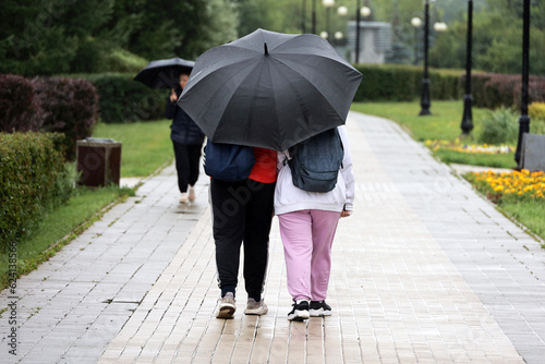 Couple with one umbrella walking on a street. Rainy weather in city, summer storm