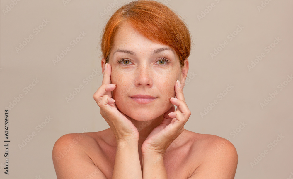 Portrait of caucasian middle aged woman of 40s with reddish hair looking at camera holding fingers on cheek , showing soft skin Portrait of caucasian middle aged woman of 40s with reddish hair looking at camera holding fingers on cheek , showing soft skin