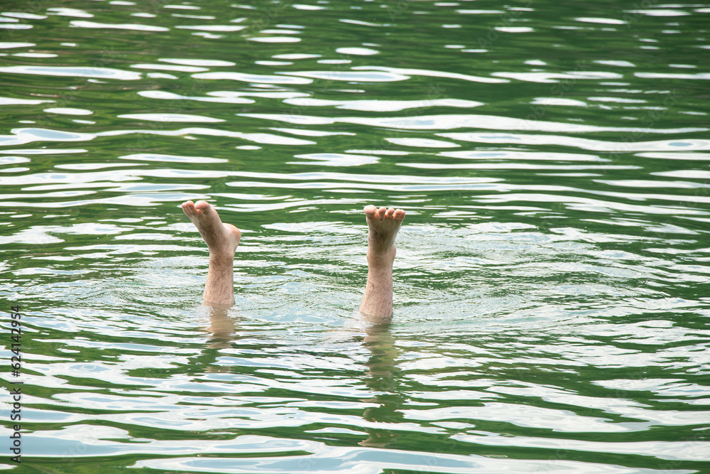 Men's legs stick out of the water in a quarry in Ukraine during swimming, feet in the water, drowning