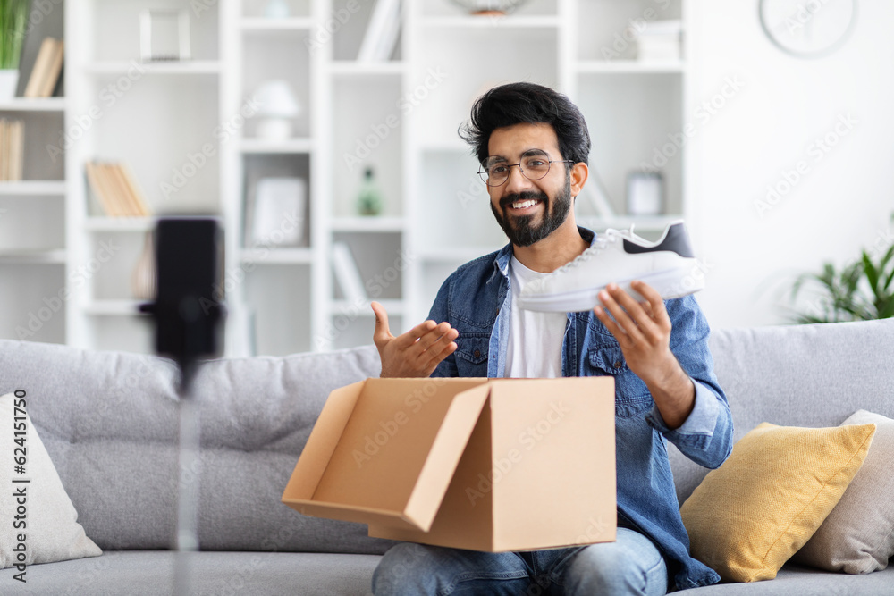 Smiling happy indian male blogger recording unboxing video for pair of shoes Smiling happy indian male blogger recording unboxing video for pair of shoes