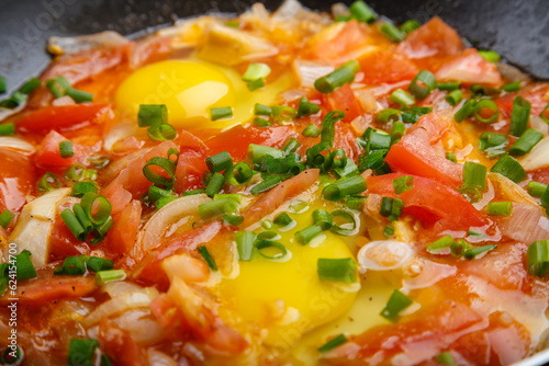 hot shakshuka sprinkled with green onions and spices close-up. photo