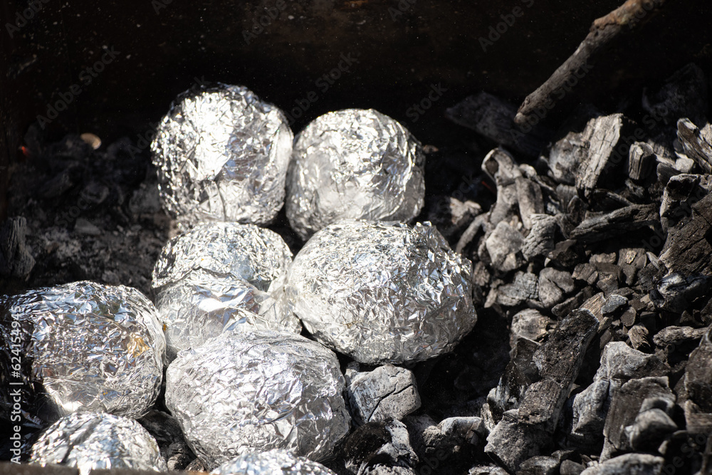 Bake potatoes in foil on the grill in the coals in the summer at a picnic, food Bake potatoes in foil on the grill in the coals in the summer at a picnic, food