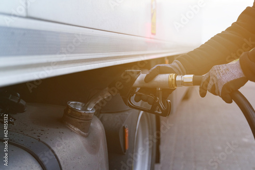 A man holds a gun in his hands, which he inserted into the neck of the fuel tank, refuels the truck.