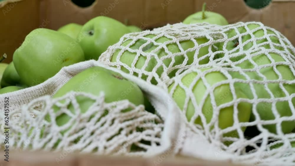 Place a mesh string bag with green apples on top of the apples in the box close-up.