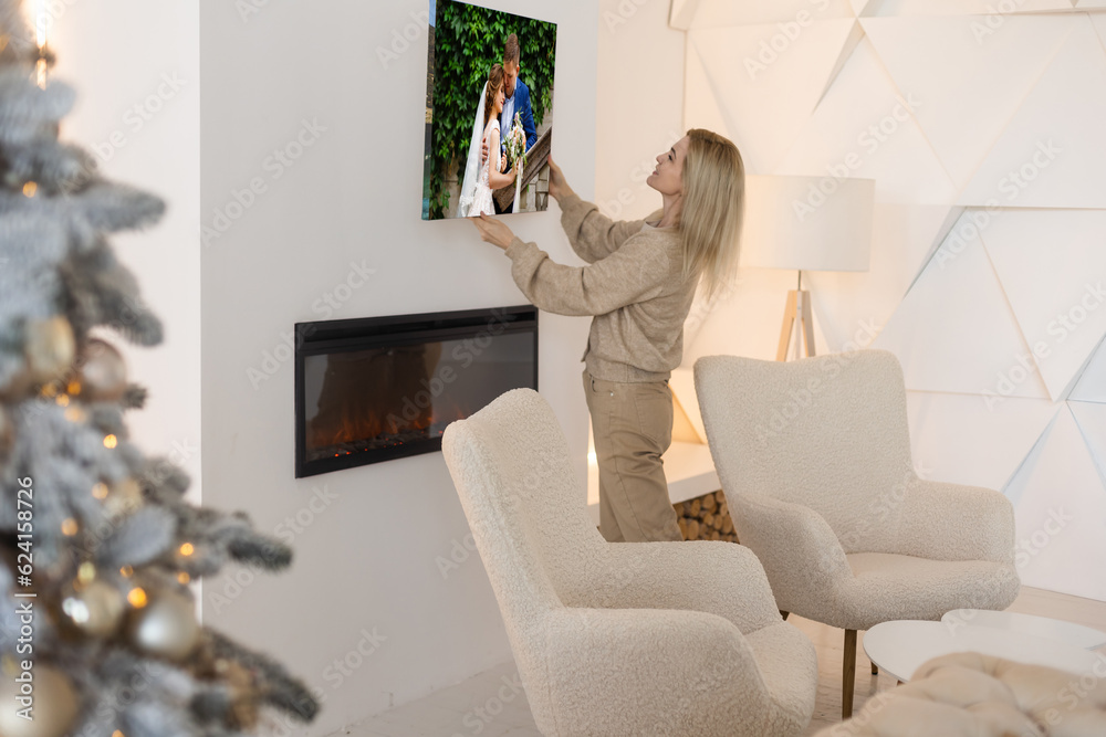 Young woman hanging a photo canvas painting on the wall Young woman hanging a photo canvas painting on the wall