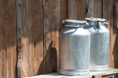 Cans of milk stand against the background of a wooden barn wall.