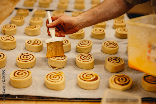 Stampa su tela baker brushes glaze onto cinnamon rolls in professional bakery kitchen