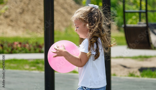 cute little girl in the summer playing outside with a ball and walking on the playground in the park, happy childhood