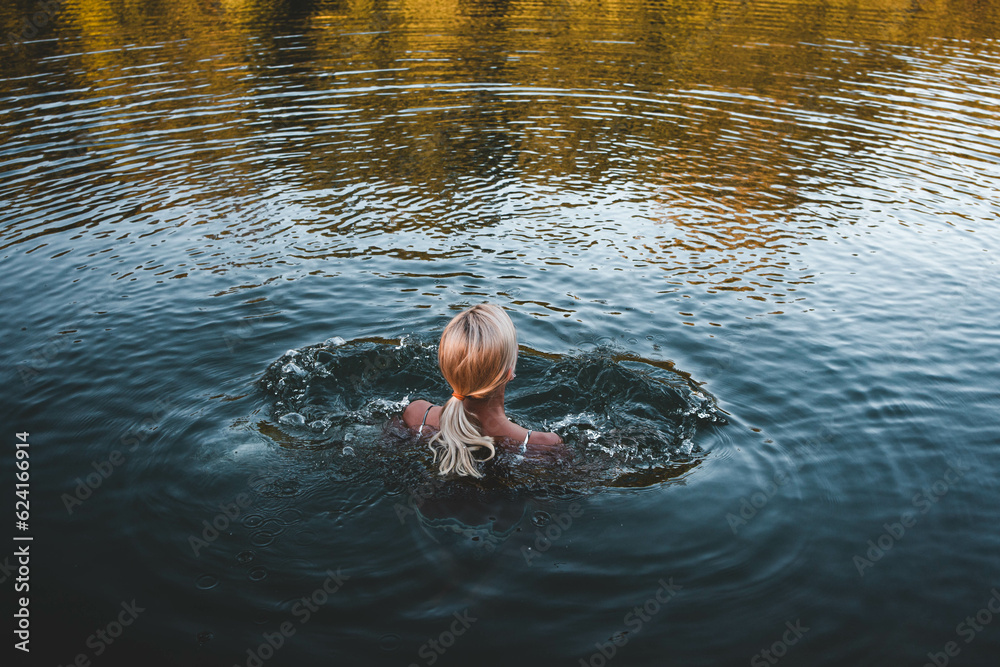 Fit blonde woman stands in the river water before entering for a swim