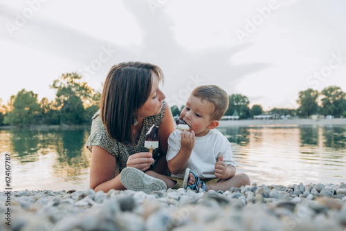 Woman with her son enjoying family time walking on the lake together , eating ice cream. Happy family parent with little child boy kid enjoy outdoor lifestyle. Mum and sun eat ice-cream