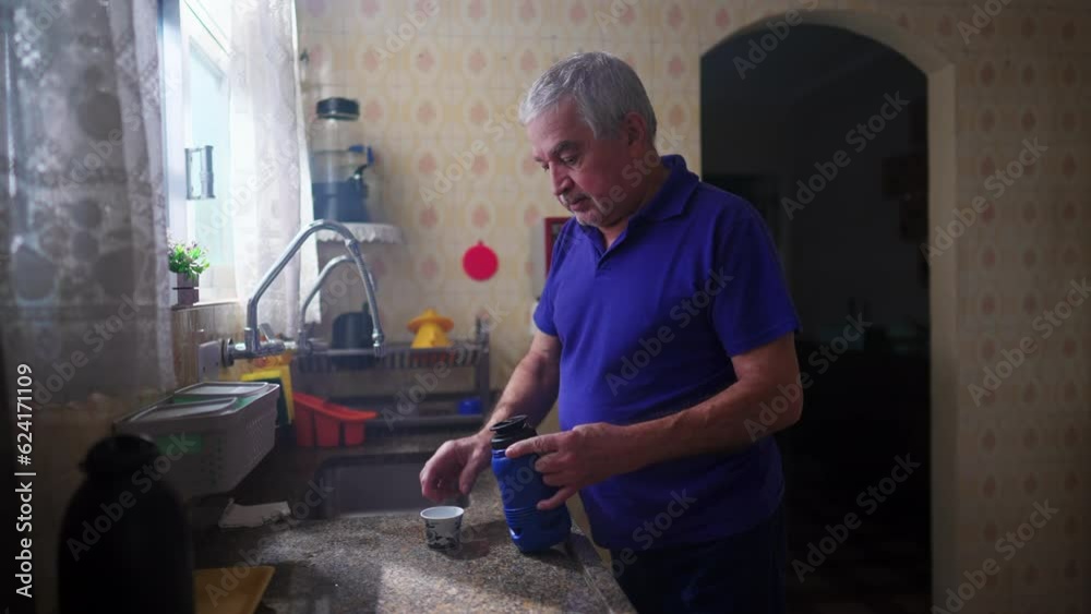Senior man standing by kitchen sink serving himself coffee and drinking in contemplation staring out window view Senior man standing by kitchen sink serving himself coffee and drinking in contemplation staring out window view