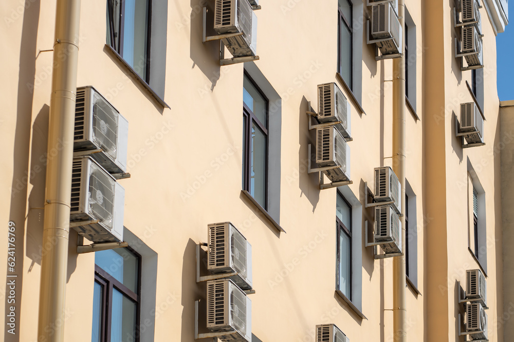 Facade of building with many air conditioners on windows in southern hot country. Yellow house exterior on city street. Escape from heat, creating favorable microclimate in urban apartments concept.