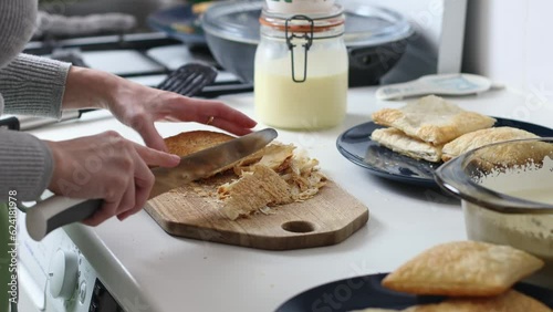 Young caucasian unrecognizable girl cuts the edges with a knife of square puff cakes on a wooden cutting board, standing at a white table in the kitchen, close-up side view.Concept step by step instru photo