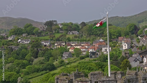 Welsh dragon flag blowing in the wind against a backdrop of a mountain side residential neighborhood, on a spring afternoon, in Conwy, Wales, UK