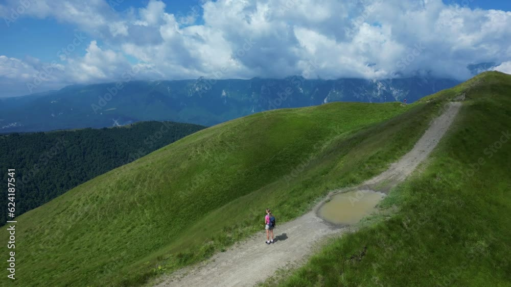 Aerial view of a young adventurous woman enjoying the view of mountain ranges. Bucegi natural park. A woman hiker with trekking equipment standing on a summit. Aerial view of a young adventurous woman enjoying the view of mountain ranges. Bucegi natural park. A woman hiker with trekking equipment standing on a summit.
