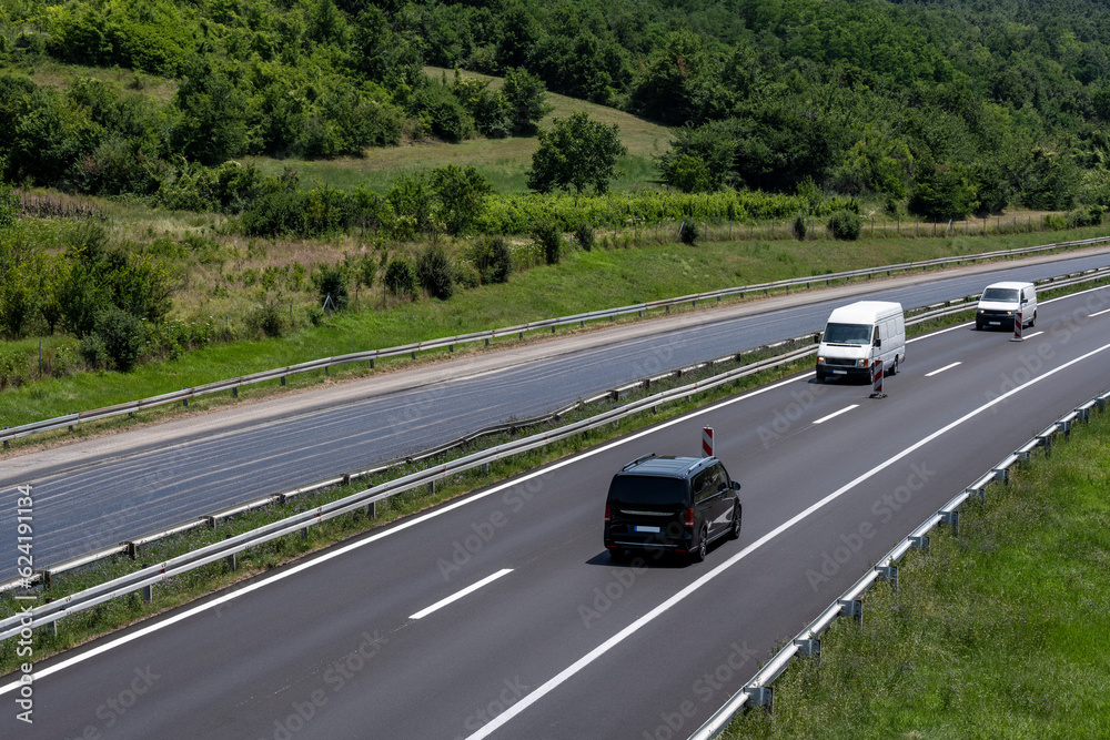 Two white Minivans and one black Minivan are moving slowly on the freeway in the opposite direction due to roadworks.
Two white Minivans and one black Minivan are moving slowly on the freeway in the opposite direction due to roadworks.