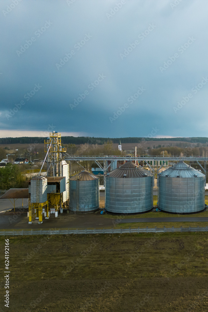 Flying a drone over silver silos on agro manufacturing plant for processing drying cleaning and storage of agricultural products, flour, cereals and grain. Large iron barrels of grain. aerial view Flying a drone over silver silos on agro manufacturing plant for processing drying cleaning and storage of agricultural products, flour, cereals and grain. Large iron barrels of grain. aerial view