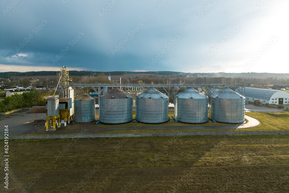 Flying a drone over silver silos on agro manufacturing plant for processing drying cleaning and storage of agricultural products, flour, cereals and grain. Large iron barrels of grain. aerial view Flying a drone over silver silos on agro manufacturing plant for processing drying cleaning and storage of agricultural products, flour, cereals and grain. Large iron barrels of grain. aerial view