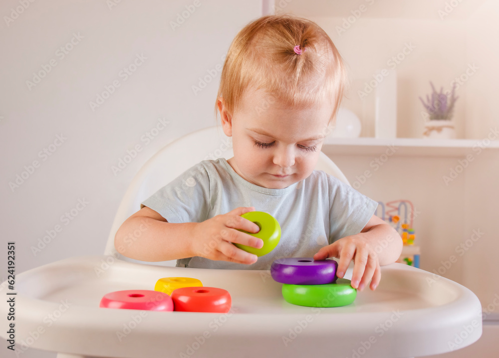 Little child plays with colorful wood toys pyramid sitting on highchair. Baby game. Games for early development Little child plays with colorful wood toys pyramid sitting on highchair. Baby game. Games for early development