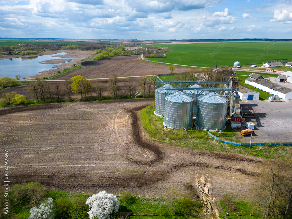 Flying a drone over silver silos on agro manufacturing plant for processing drying cleaning and storage of agricultural products, flour, cereals and grain. Large iron barrels of grain. aerial view Flying a drone over silver silos on agro manufacturing plant for processing drying cleaning and storage of agricultural products, flour, cereals and grain. Large iron barrels of grain. aerial view