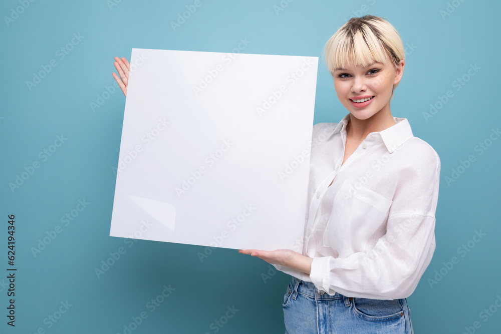 young successful pretty blond office worker woman in a white shirt and jeans holds a piece of paper to insert an advertisement. business concept young successful pretty blond office worker woman in a white shirt and jeans holds a piece of paper to insert an advertisement. business concept