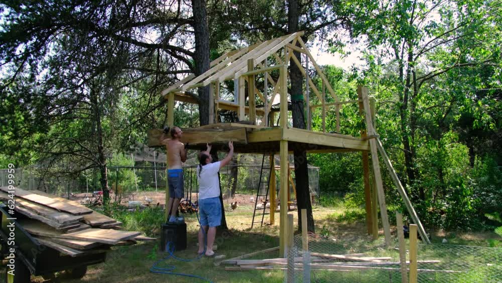 Two men mounting plank cut from own lumber onto side of tree house making siding for wall with cozy look. Two men mounting plank cut from own lumber onto side of tree house making siding for wall with cozy look.