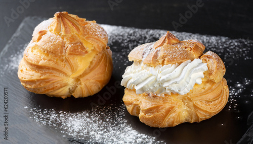 Cream puffs with whipped cream is a classic French dessert also called choux pastry, on black slate board, dusted with sugar powder.