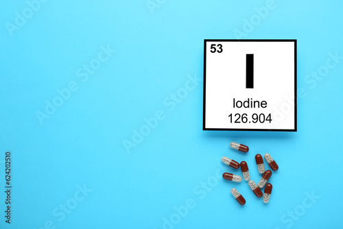 Foto Card with iodine element and pills on light blue background, flat lay