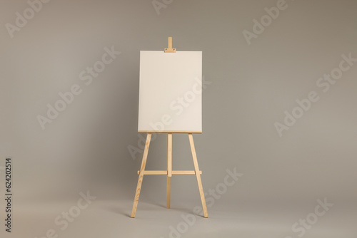 Wooden easel with blank canvas on grey background