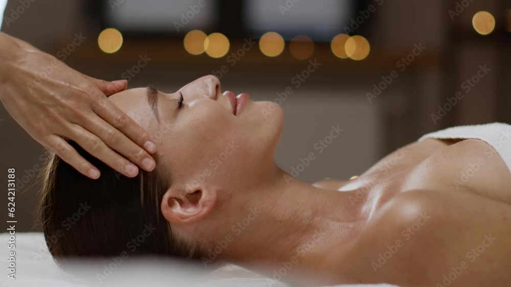 Side view portrait of young peaceful lady enjoying head massage by professional masseur hands at spa center