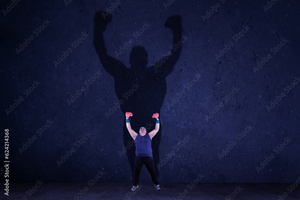 Overweight man with boxing glove raising hands after exercise