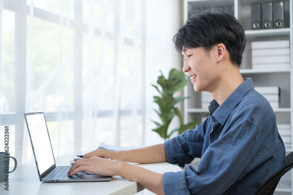 Side view of young start up businessman using laptop computer at desk in modern workplace. Side view of young start up businessman using laptop computer at desk in modern workplace.
